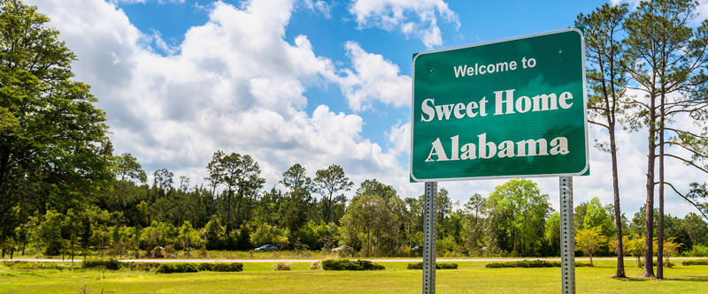 Rural highway with green sign that says "Welcome to Sweet Home Alabama"